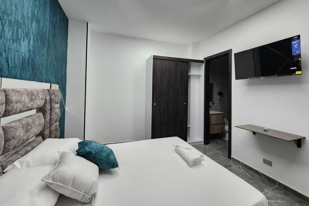 A modern hotel room with a bed, a TV mounted on the wall, and a door leading to the bathroom.