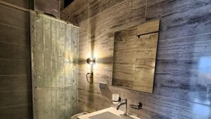 Un baño moderno con cabina de ducha de vidrio, inodoro, lavabo con espejo y una pared con textura de madera.