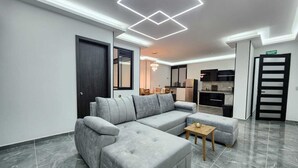 Una sala moderna con un sofá modular, una mesita de centro pequeña y una cocina al fondo.