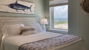 Et soveværelse med seng, et vindue med udsigt, en lampe og et billede af en fisk på væggen.