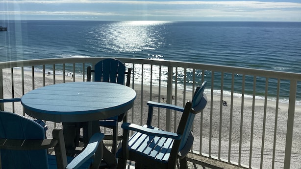 En balkon med et bord og stole med udsigt over en strand og hav.