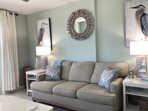 A living room with a sofa, two side tables, a mirror, and artwork. - Beautiful gulf front 2 bedroom 2 bath steps to the water (Gulf Shores)