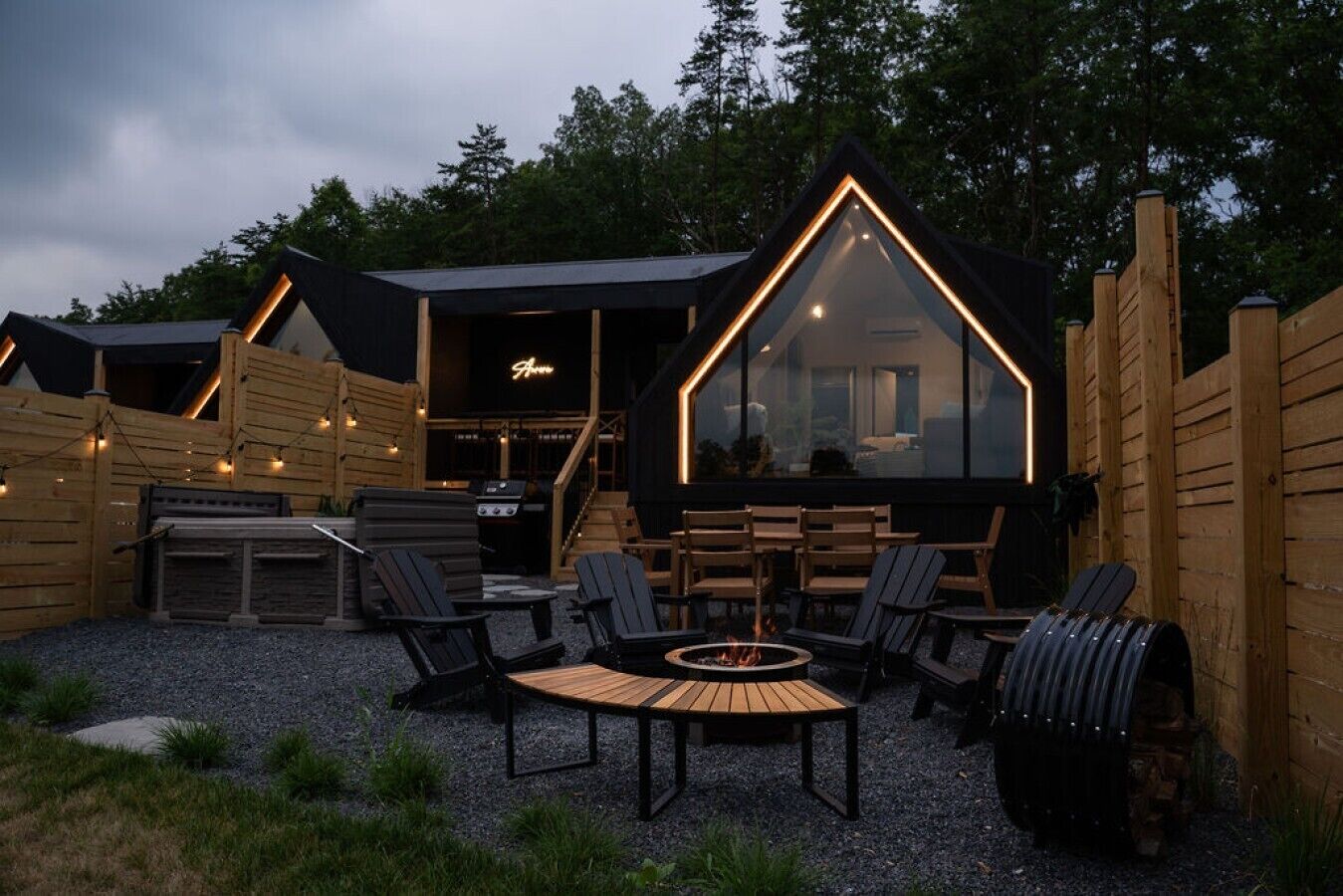 A cozy outdoor seating area with a fire pit, wooden furniture, and a large glass window.