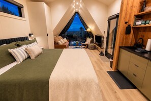 Ein Schlafzimmer mit einem großen Bett, Blick durch ein Fenster, einer Küchenzeile und einer Sitzecke.