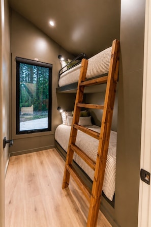 Una stanza con un letto a castello, una scala in legno, una finestra con vista su una foresta e una porta.
