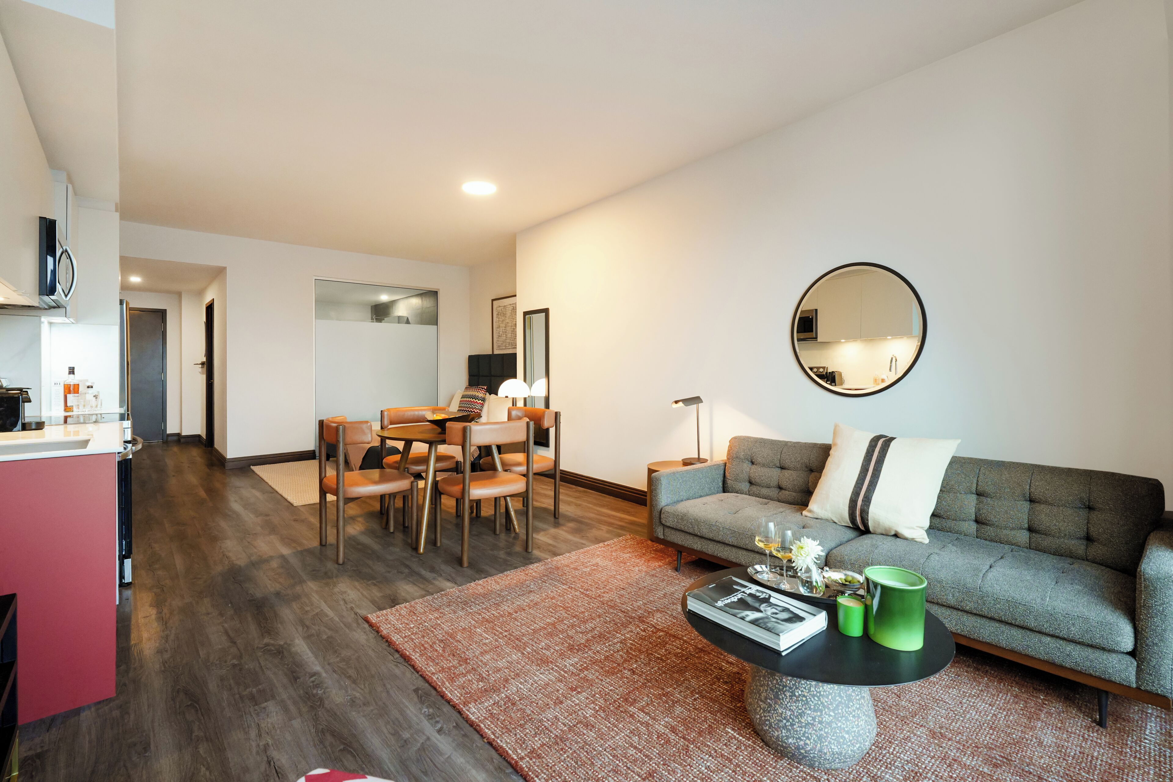 A modern living room with a grey sofa, round coffee table, and a dining area with a wooden table and chairs.