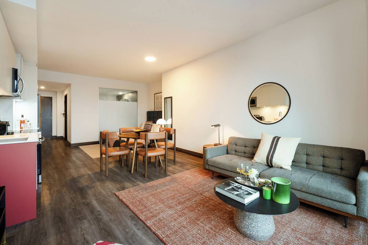 A modern living room with a grey sofa, round coffee table, and a dining area with a wooden table and chairs.