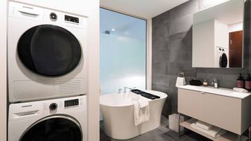 A modern bathroom with a washing machine, a freestanding bathtub, and a vanity with a mirror.