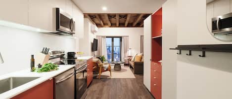 A modern kitchen with built-in appliances, a dining area with a sofa and table, and a view through a window.