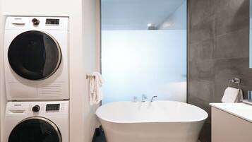 Un baño moderno con lavadora y secadora integradas, una bañera independiente y un ventanal amplio.