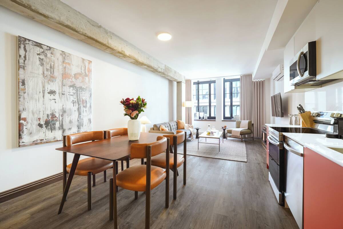 A modern kitchen with a dining area, a large abstract painting, and a view through the window.