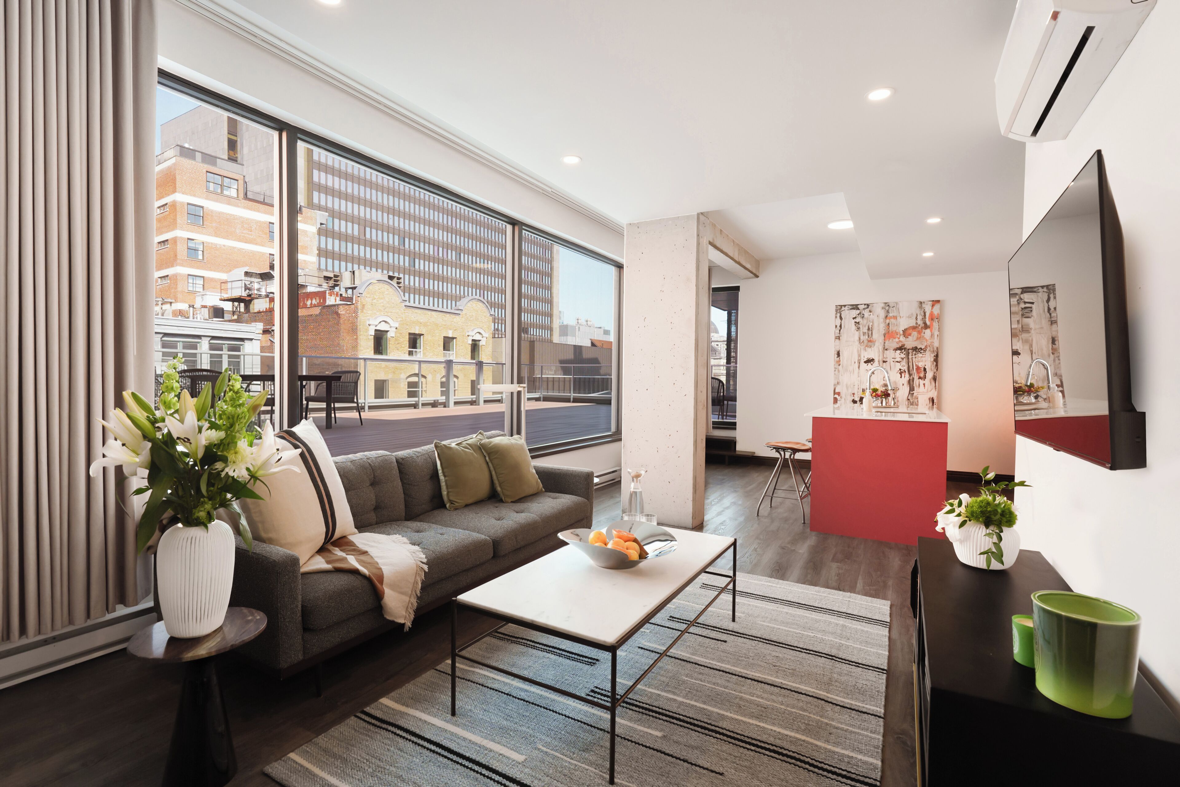 Un salon moderne avec un canapé, une table basse et une vue sur la ville grâce à de grandes fenêtres.