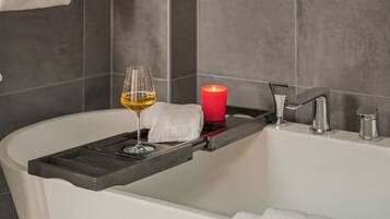 A bathtub with a tray holding a glass of wine and a candle.