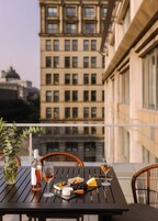 Un balcon avec une table dressée pour un repas, comprenant une bouteille, des verres à vin, du fromage et des olives.