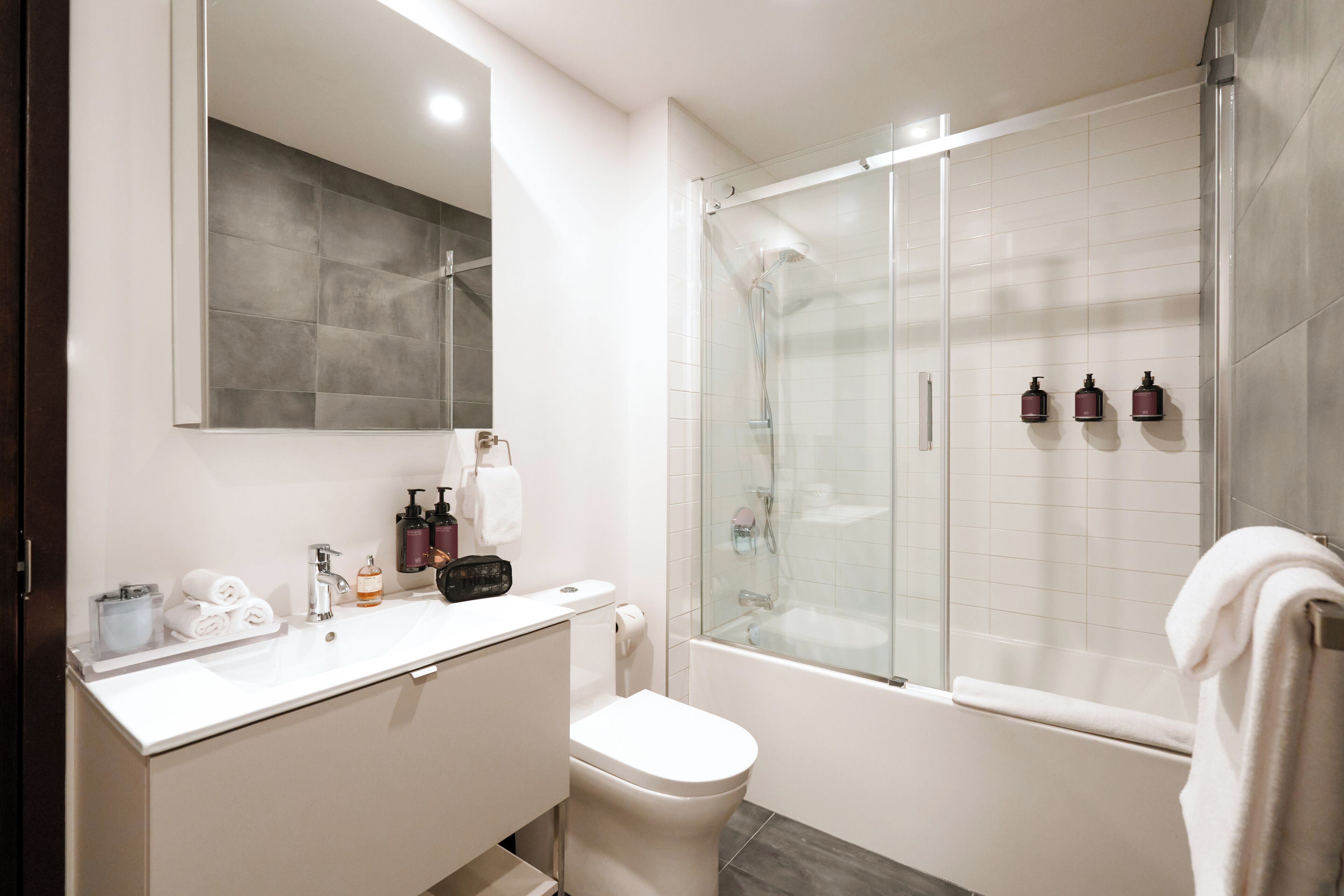 Un baño moderno con ducha envuelta en vidrio, un lavamanos blanco y un espejo grande.