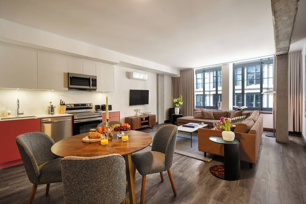 A modern living room with a dining area, kitchen, and large windows.