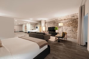 A modern hotel room with a large bed, a sofa, a TV, and a stone wall. - Brésoles Hotel (Montréal)