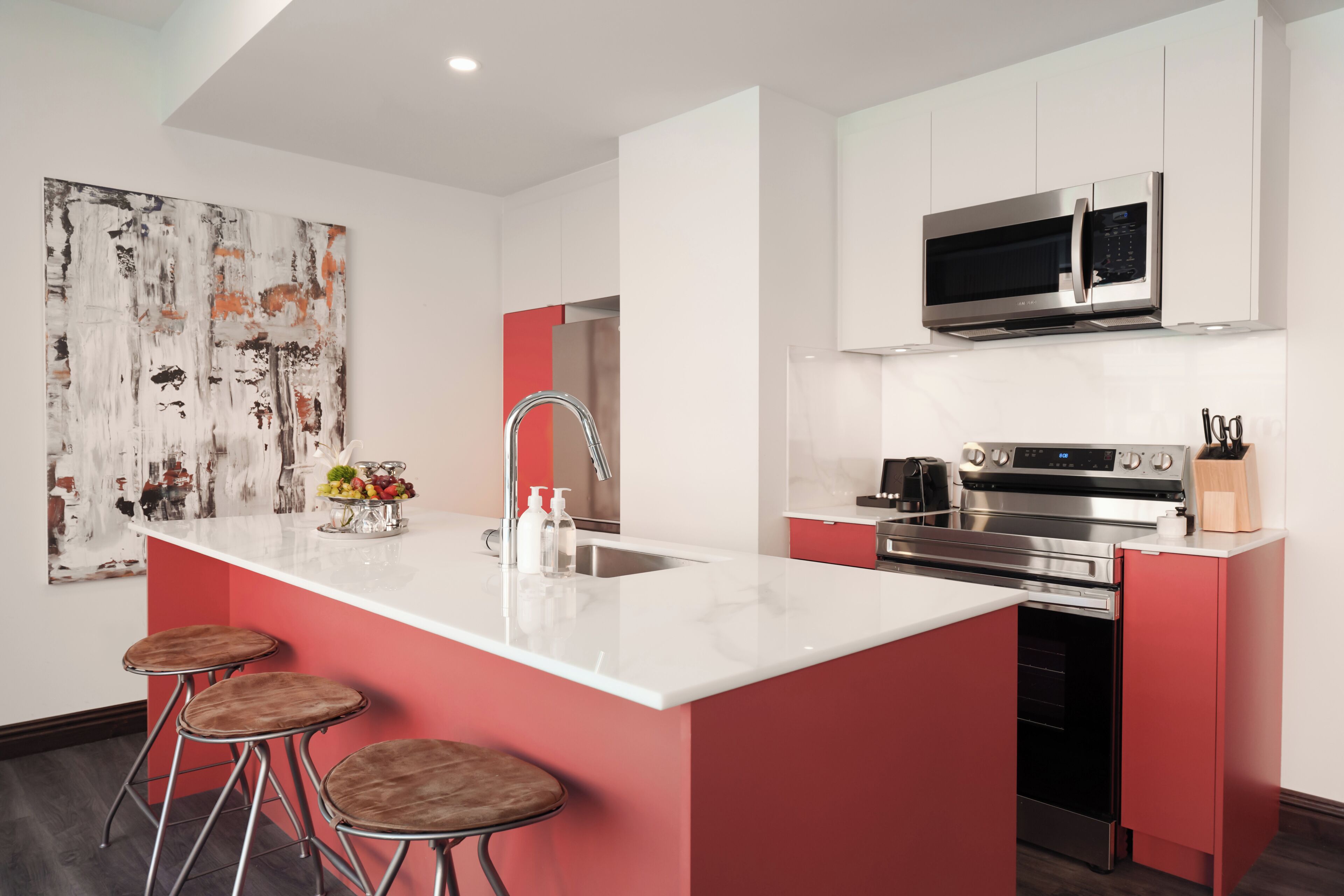 A modern kitchen with a central island, stainless steel appliances, and a red accent wall.