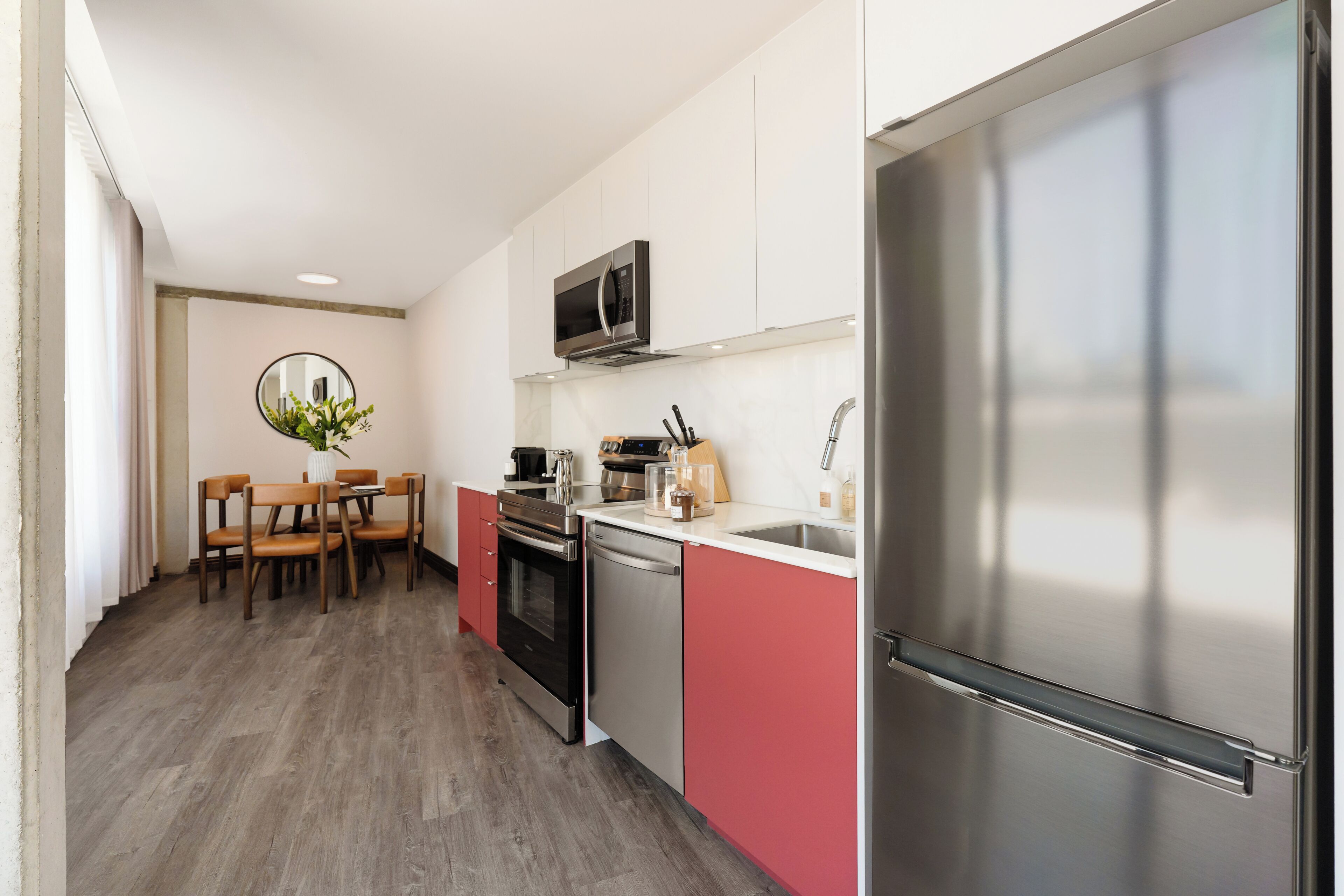A modern kitchen with stainless steel appliances, a dining area with wooden chairs, and a round mirror on the wall.