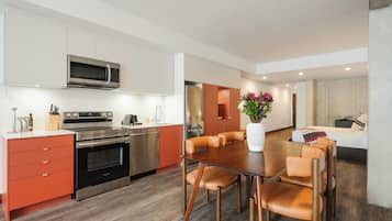 A modern kitchen with stainless steel appliances, a dining area with wooden chairs, and a living space with a sofa and a decorative vase.