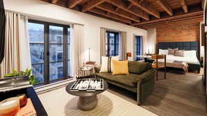Ein Hotelzimmer mit Holzboden, einer Couch, einem Bett, einem kleinen Tisch und Blick durch große Fenster.