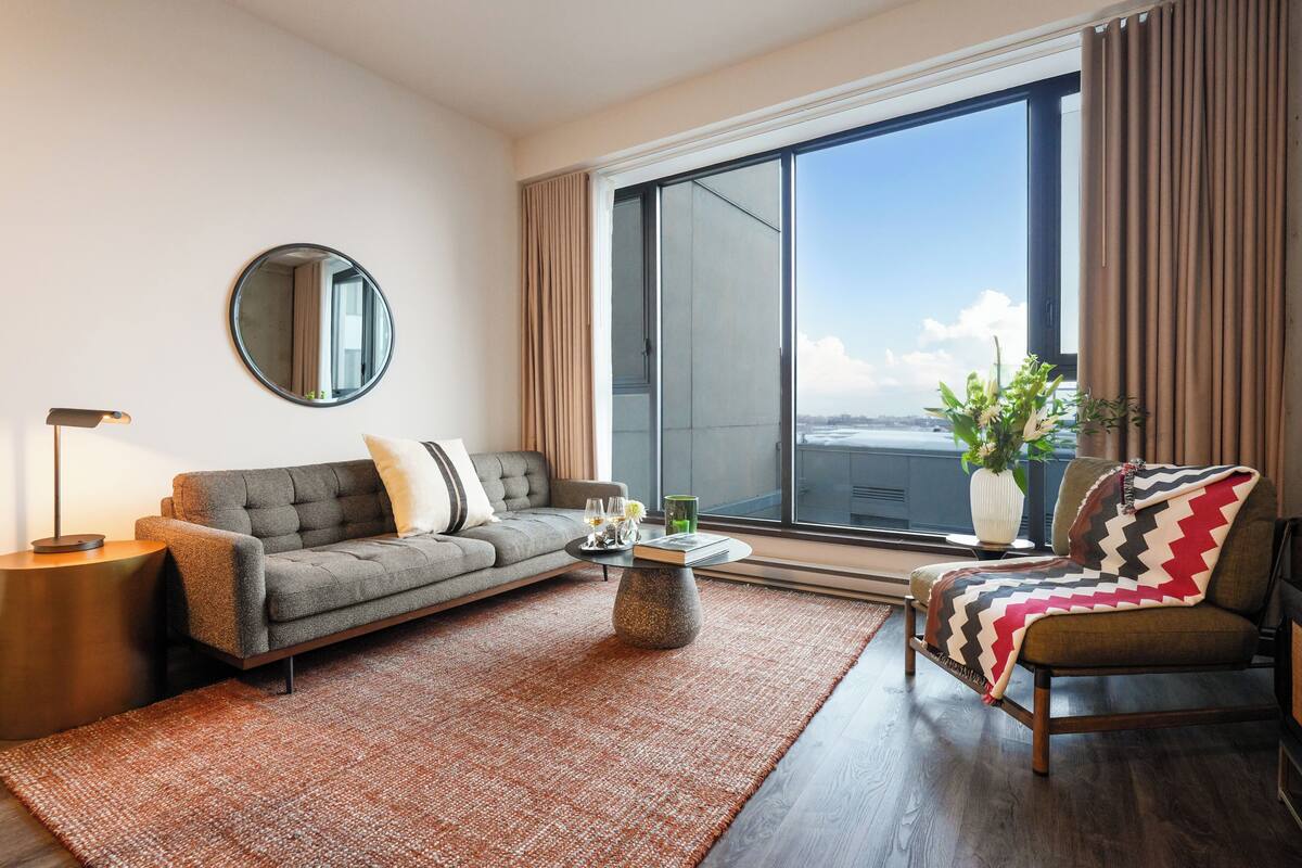A modern living room with a sofa, armchair, coffee table, and a large window with curtains.
