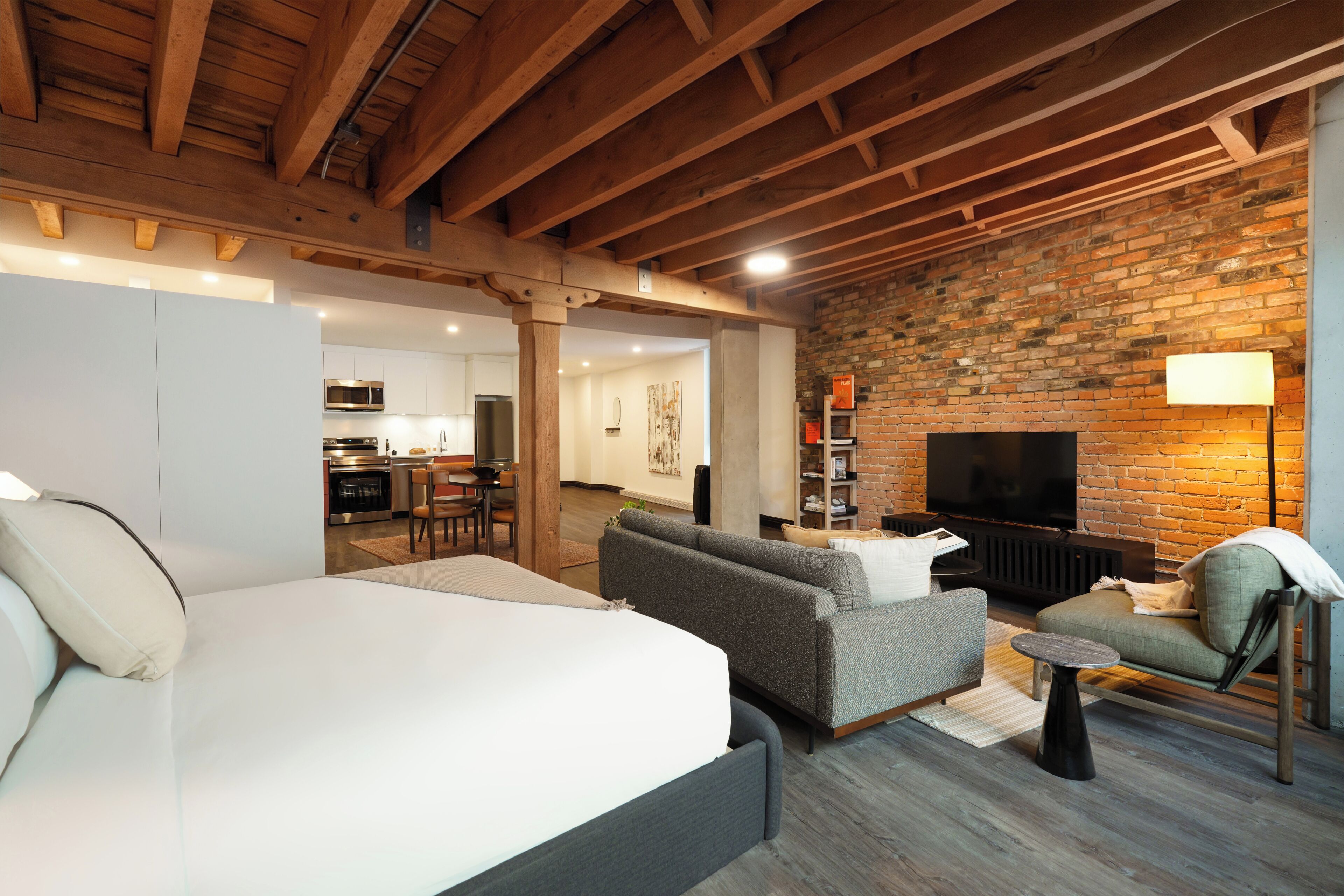 A modern living room with a large bed, sofas, a TV, and a brick wall.