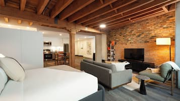 A modern living room with a large bed, sofas, a TV, and a brick wall.