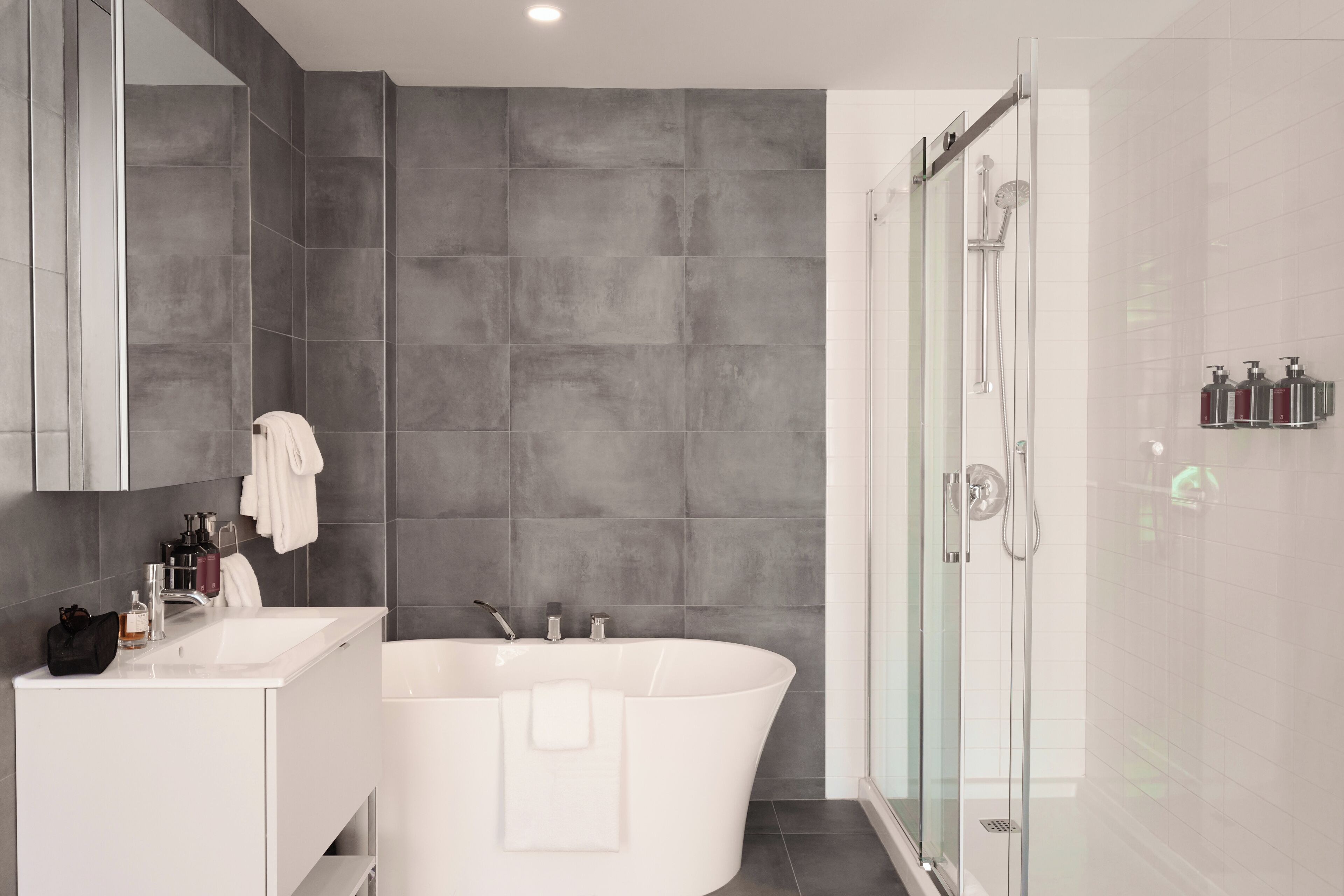 Un baño moderno con una bañera independiente, cabina de ducha con mampara de vidrio y tocador con espejo.