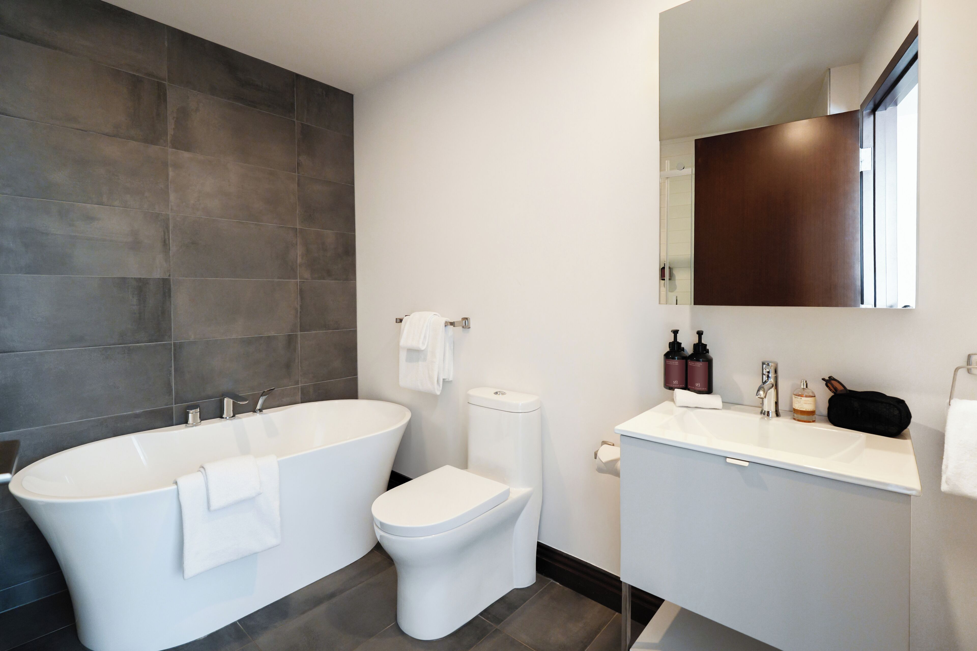 A modern bathroom with a freestanding bathtub, a toilet, and a vanity with a mirror.