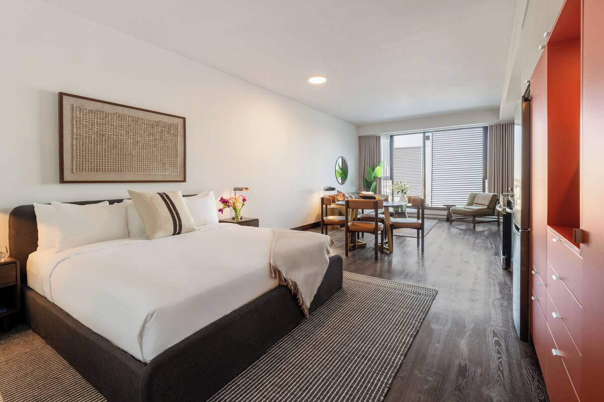 A hotel room with a large bed, a desk, a chair, and a view of the outdoors.