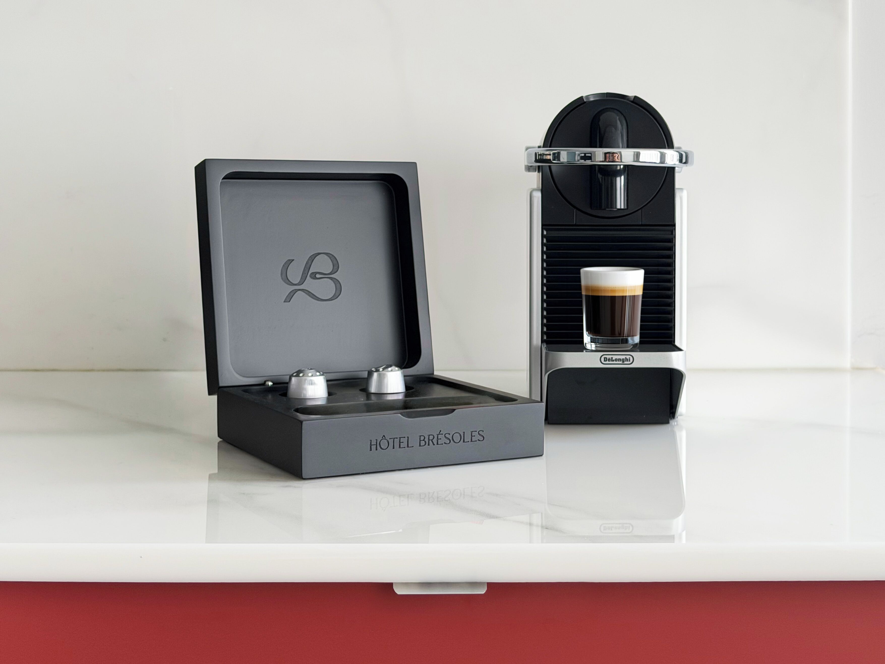 Une machine à café, une tasse de café et une boîte étiquetée « HÔTEL BRÉSOLES ».