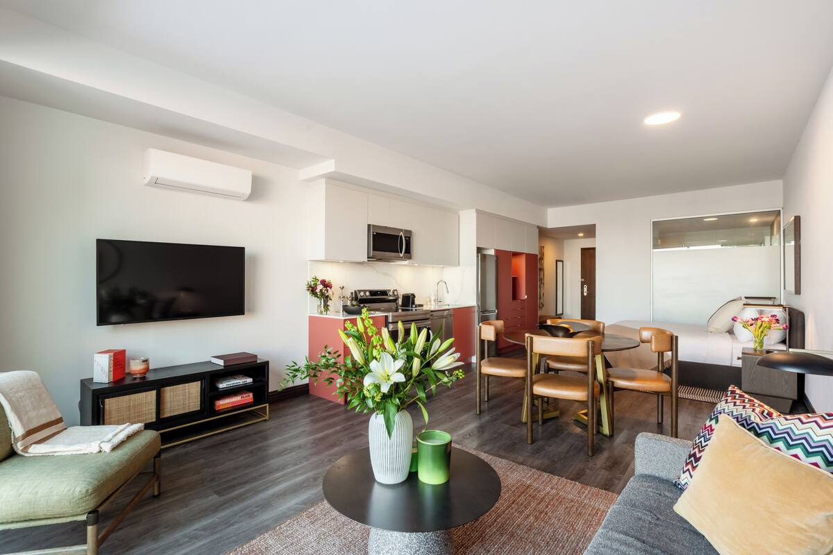 A modern living room with a flat-screen TV, a dining area, a kitchen, and a sofa.