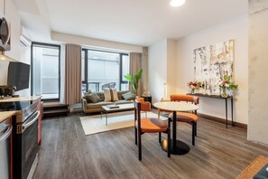 A modern living room with a sofa, dining table, chairs, a TV, and a large window. - Brésoles Hotel (Montréal)