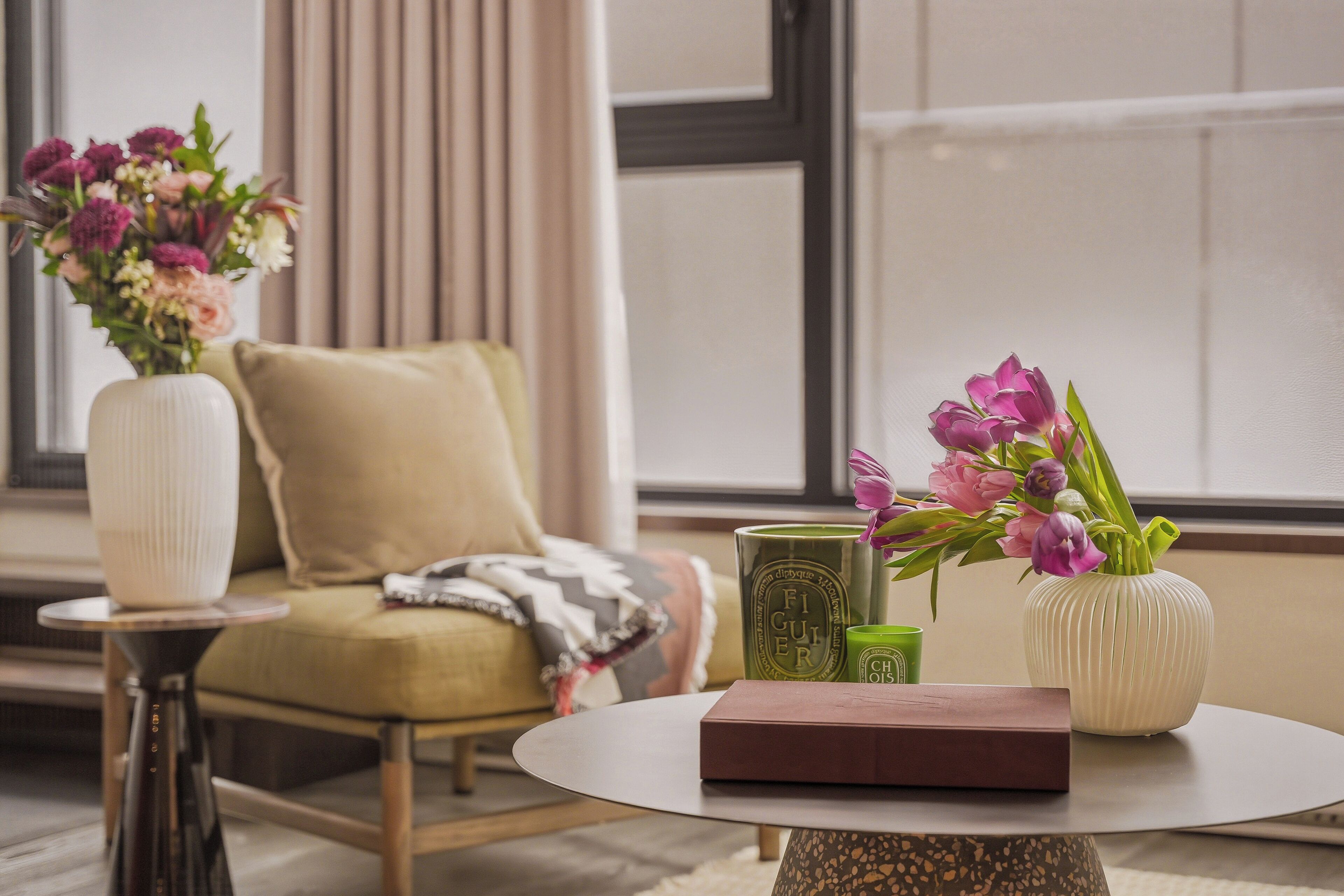 Ein Zimmer mit einer Couch, einem runden Tisch, einer Vase mit Blumen und einem grünen Kerzen.