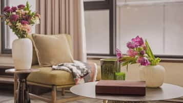 Ein Zimmer mit einer Couch, einem runden Tisch, einer Vase mit Blumen und einem grünen Kerzen.