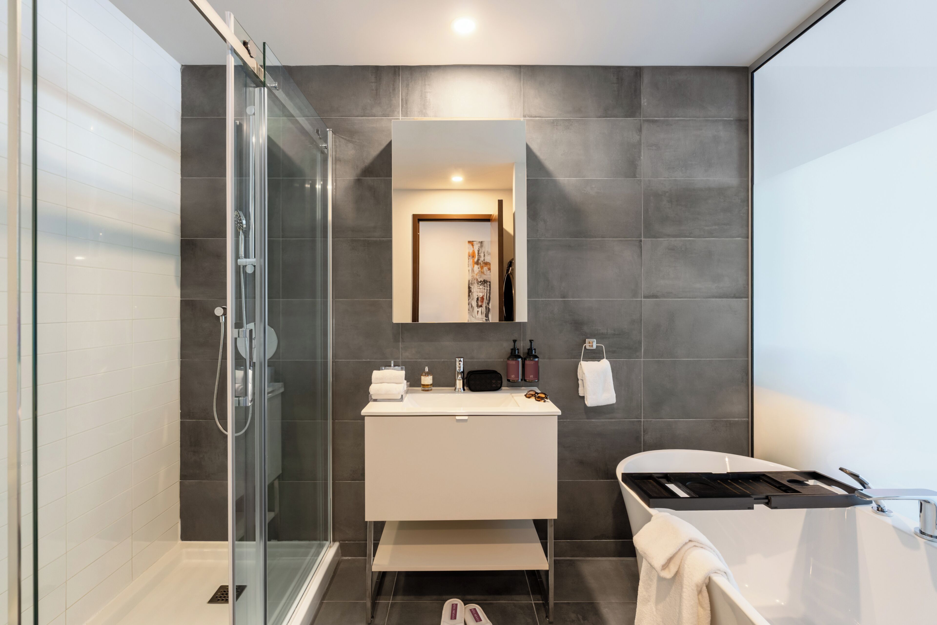 A modern bathroom with a glass shower enclosure, a white vanity, a large mirror, and a bathtub.