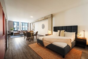 A modern hotel room with a large bed, a dining area, and a view of the city. - Brésoles Hotel (Montréal)