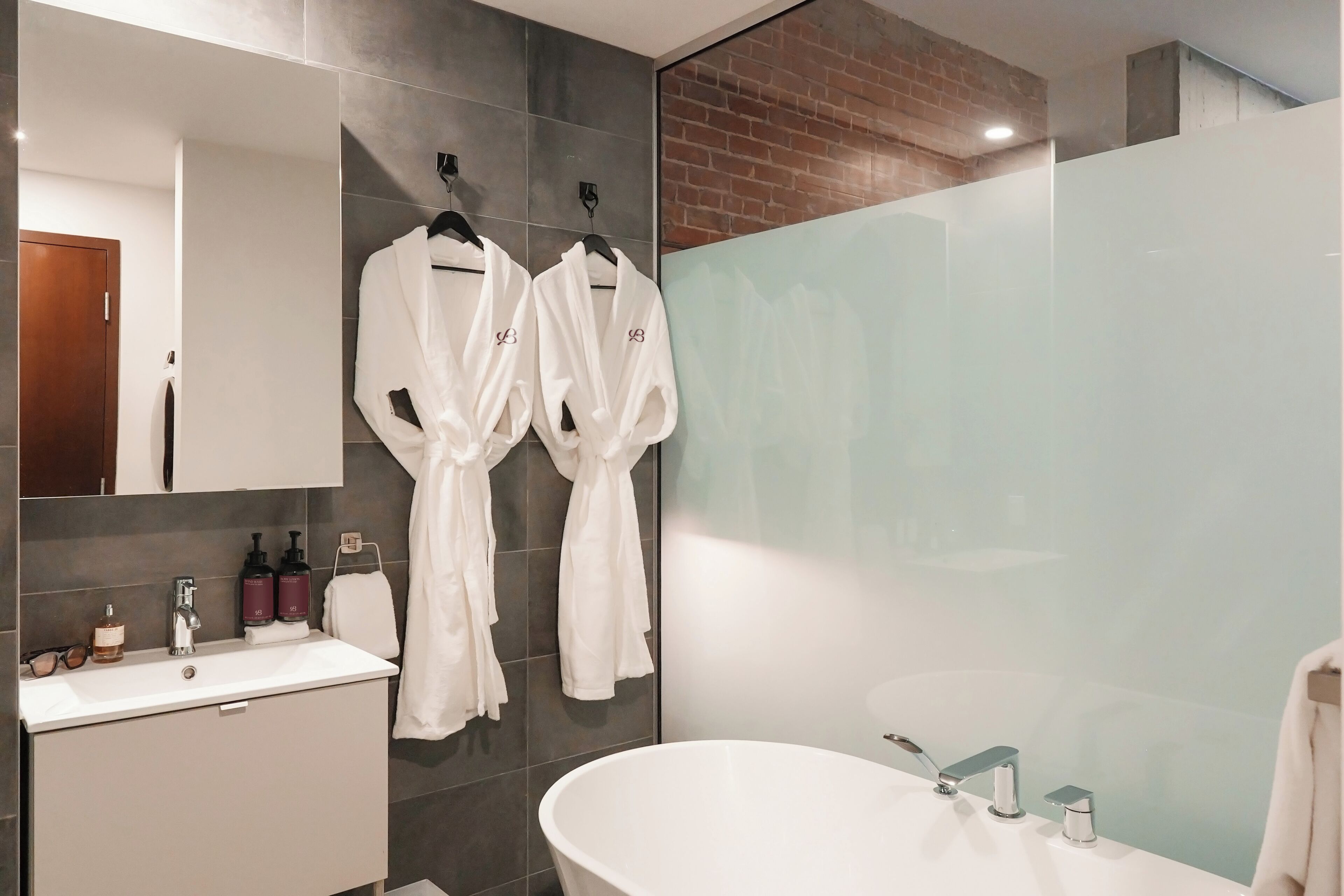 A modern bathroom with a white sink, a large mirror, and two white robes hanging on a rack.