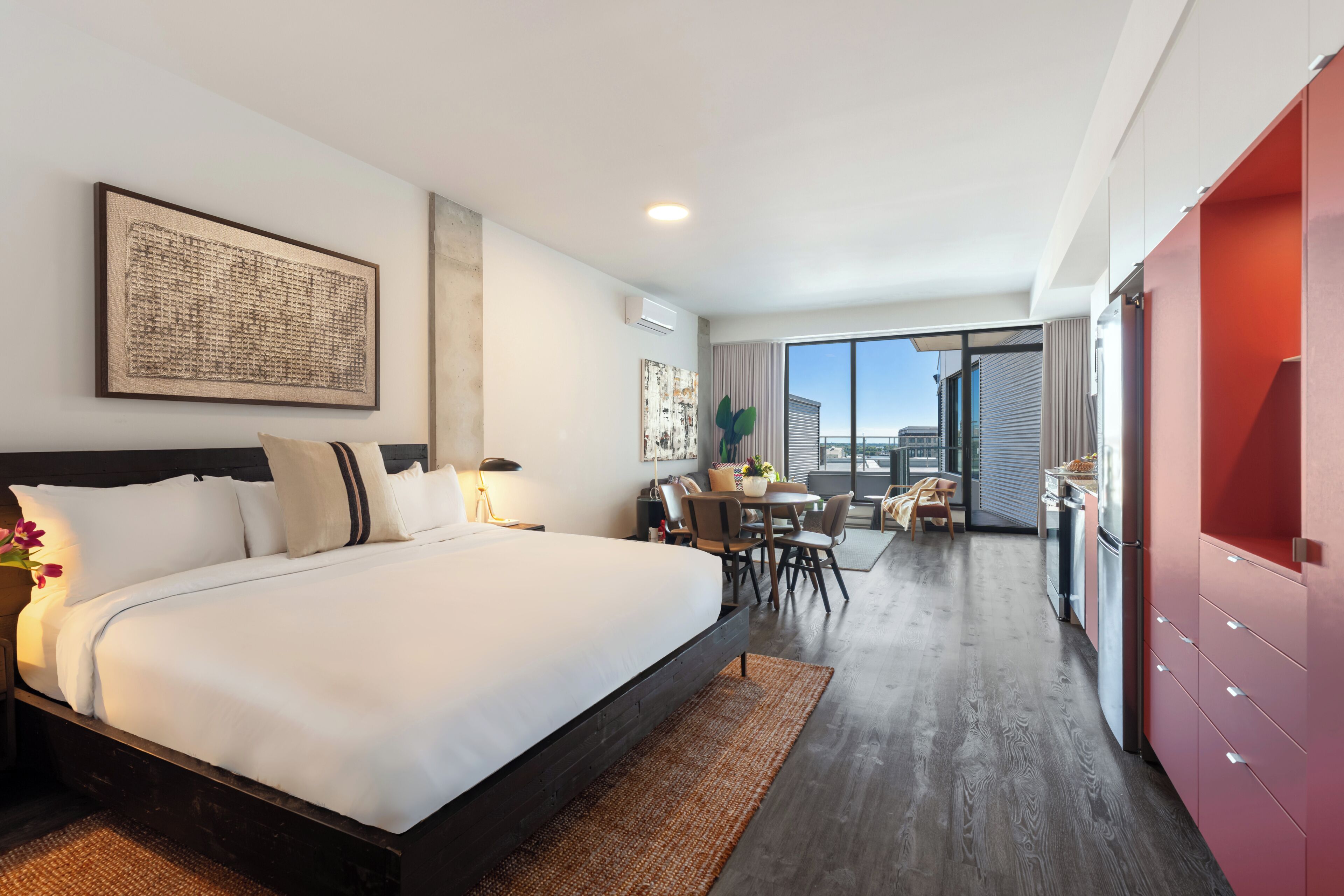 A modern hotel room with a large bed, a dining area, and a view of the city.