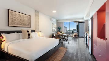 A modern hotel room with a large bed, a dining area, and a view of the city.