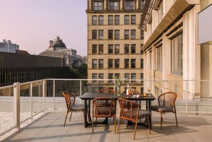 A terrace with a table and chairs, overlooking a cityscape with historic buildings.