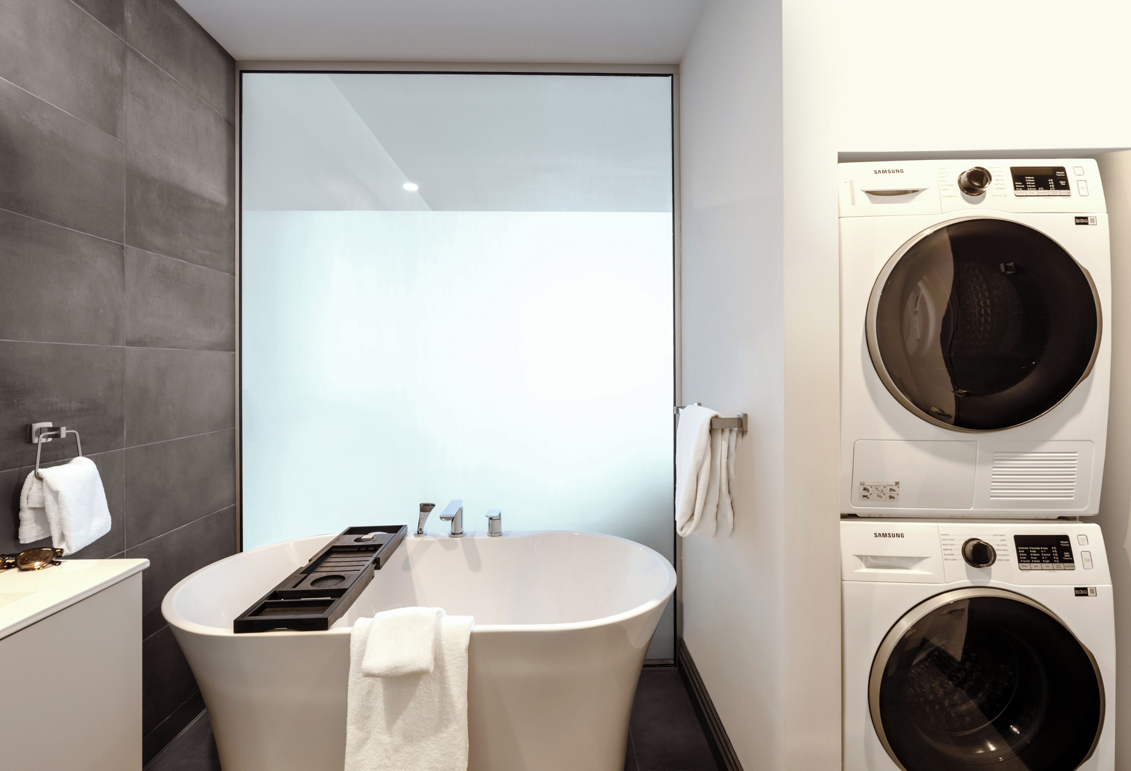 A modern bathroom with a freestanding bathtub, a built-in washing machine, and a large mirror.