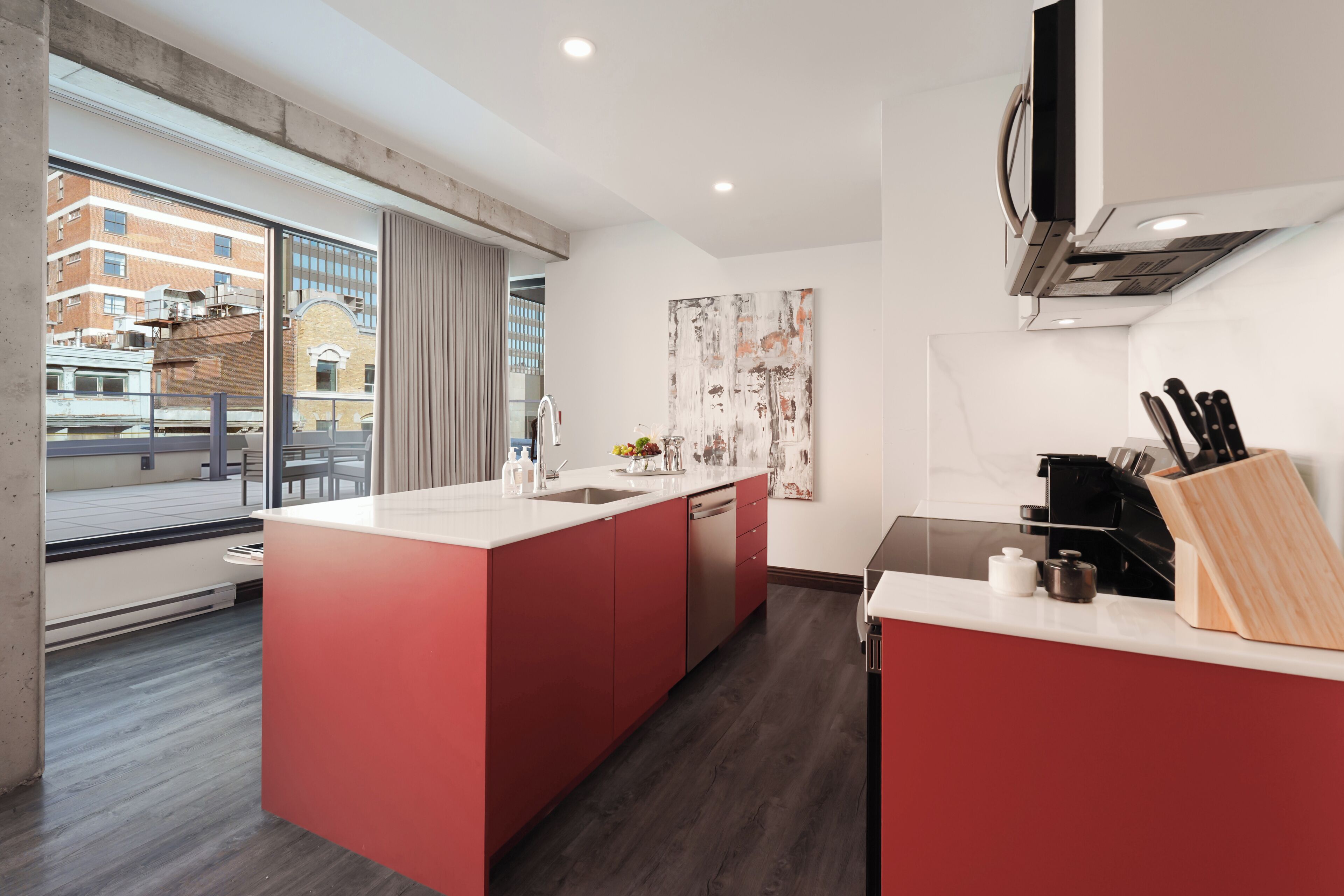 A modern kitchen with a central island, a built-in dishwasher, and a view of the city through large windows.