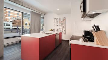A modern kitchen with a central island, a built-in dishwasher, and a view of the city through large windows.
