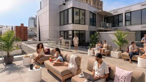 Eine Dachterrasse mit Sitzgelegenheiten im Freien, ein modernes Gebäude im Hintergrund und ein klarer Himmel.