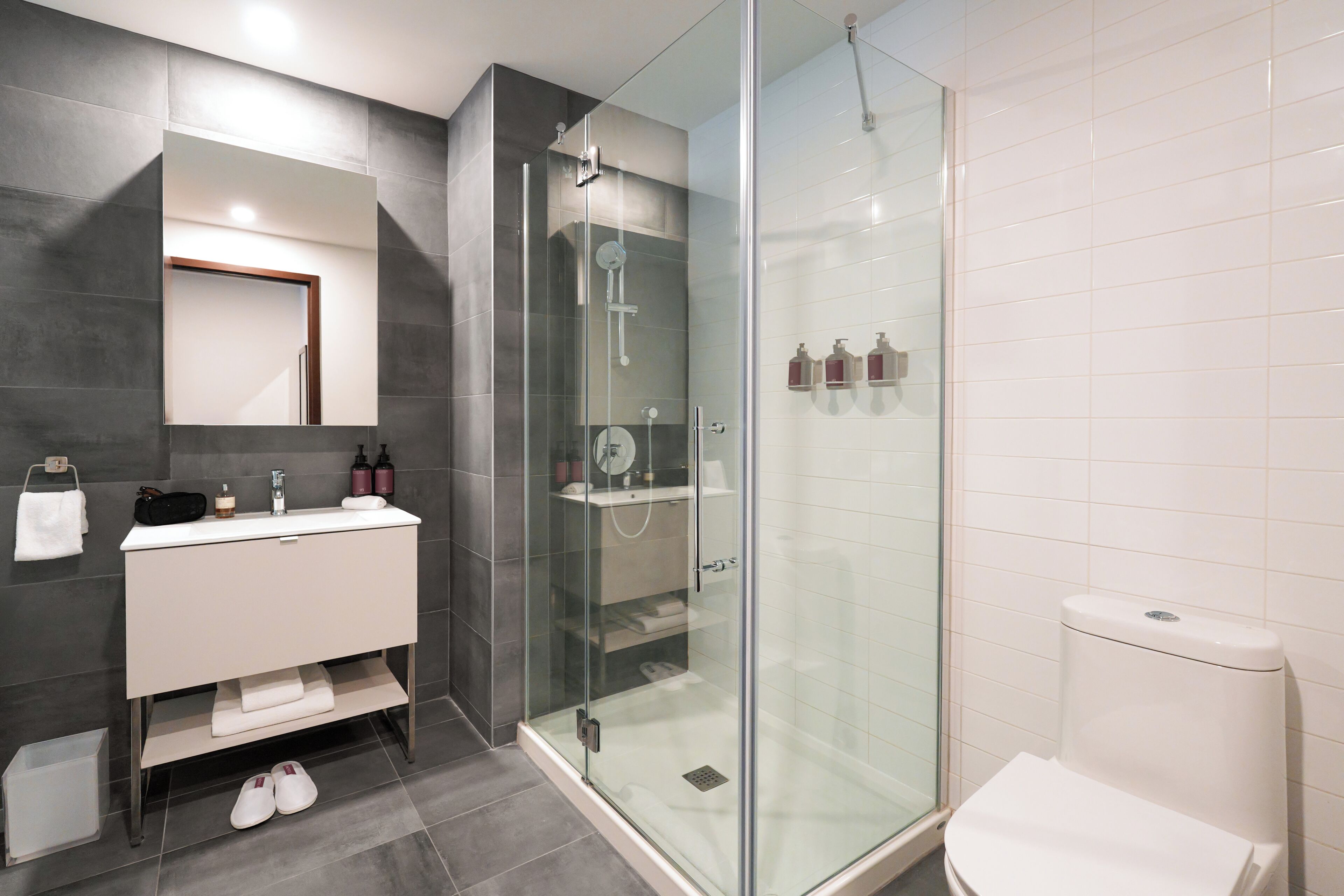 Un baño moderno con ducha de vidrio, un lavabo blanco con espejo y un inodoro.