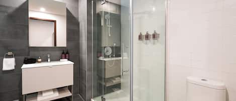 A modern bathroom with a glass-enclosed shower, a white sink with a mirror, and a toilet.