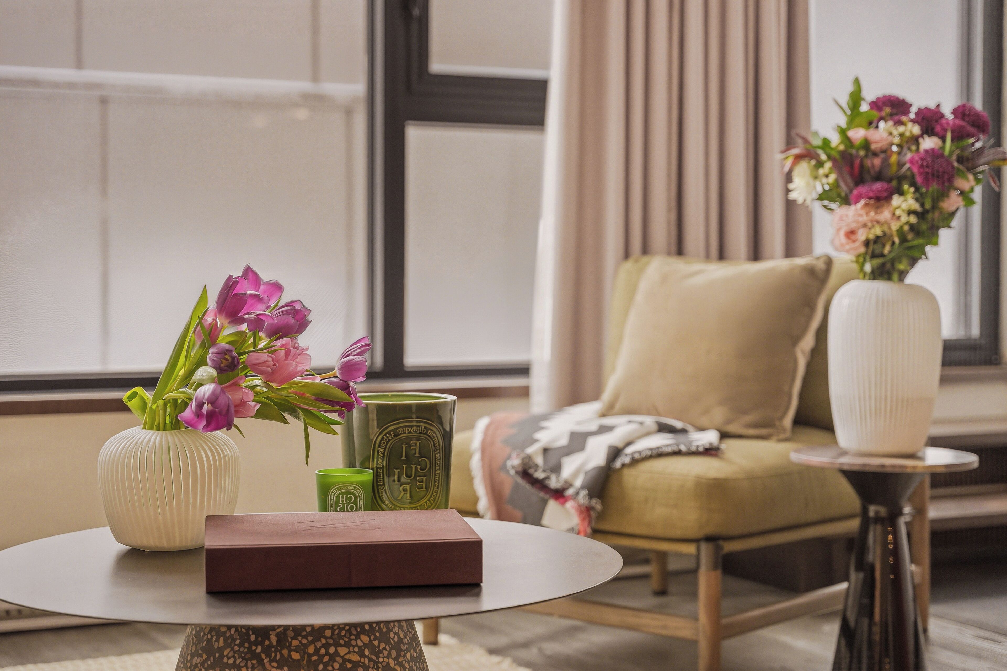 A room with a round table, a chair, a vase with flowers, and a book.