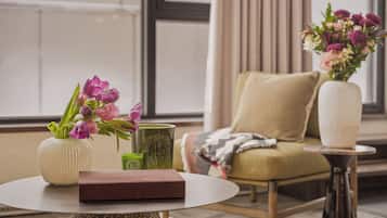 A room with a round table, a chair, a vase with flowers, and a book.